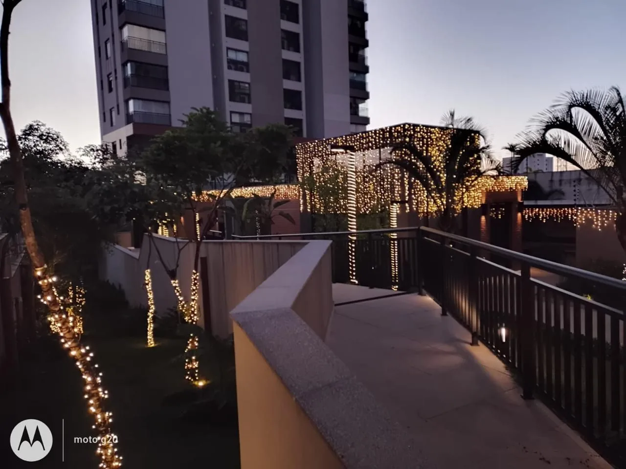 Passarela do condomínio com luz nas árvores e no guarda-corpo